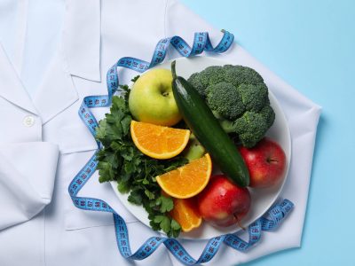 Doctors coat, healthy food and measuring tape on blue background - weight loss